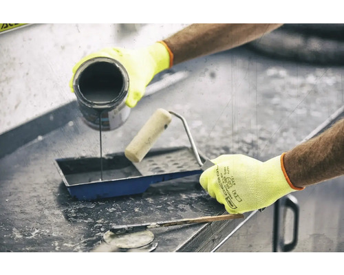 Eine Person gießt Farbe in eine Farbwanne neben einer Farbrolle und einem Spachtel