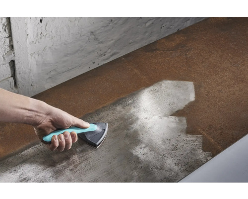 Hand mit Dreiecksschaber beim Reinigen einer Metalloberfläche