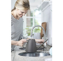 Frau befüllt eine graue Gießkanne an einem Wasserhahn