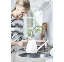 Frau füllt eine weiße Gießkanne am Wasserhahn in der Küche.