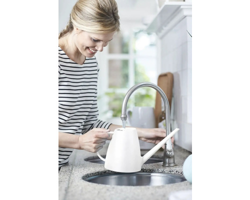 Frau füllt eine weiße Gießkanne am Wasserhahn in der Küche.