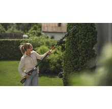 Frau schneidet Hecke mit einer Heckenschere mit Stiel im Garten.