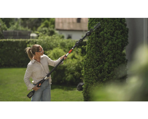 Frau schneidet Hecke mit einer Heckenschere mit Stiel im Garten.