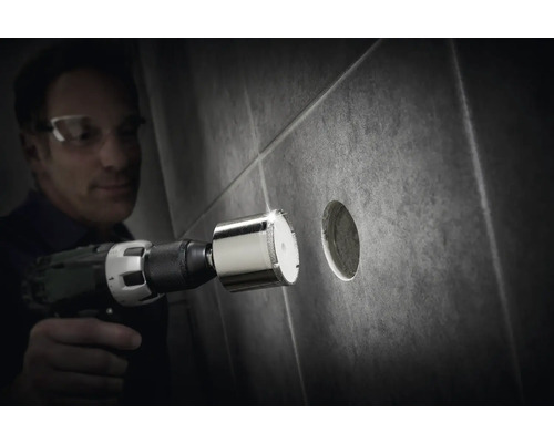 Mann bohrt mit einer Diamantbohrkrone ein Loch in eine Fliese.