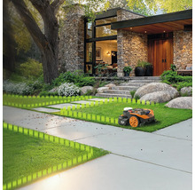 Ein Rasenmähroboter auf einem Rasen vor einem Haus mit Steinfassade und großem Baum.