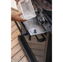 Wasser wird in die Fettauffangschale eines Grills gegossen.