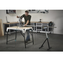 Mann arbeitet mit einer Bohrmaschine an einem Werktisch, im Hintergrund Werkzeuge und eine Werkbank.