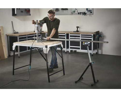 Mann arbeitet mit einer Bohrmaschine an einem Werktisch, im Hintergrund Werkzeuge und eine Werkbank.