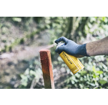 Eine Person sprüht mit einer gelben Universalspraydose einen Holzpfosten an