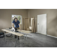 Mann schneidet Holz mit einer Handkreissäge auf einer Werkbank in einem Raum.