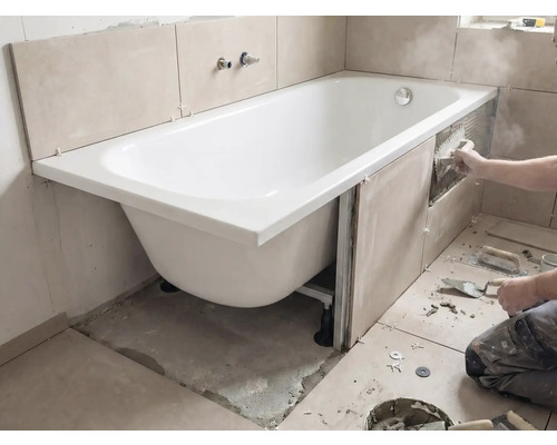 Installation einer Badewanne mit Fliesen an den Wänden und Werkzeugen im Badezimmer.