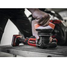 Ein Mann poliert ein Auto mit einer Poliermaschine. Die Poliermaschine ist rot und schwarz und hat ein Polierpad.