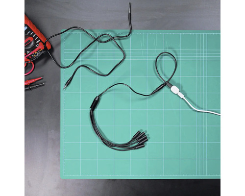 Verteilerkabel mit fünf Anschlüssen auf einer Schneidematte neben einem Multimeter und weiteren Kabeln in einer organisierten Arbeitsumgebung.