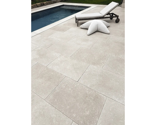 Moderne Terrasse mit großformatigen Steinplatten neben einem Swimmingpool, inklusive Gartenliege und sternförmigem Sitzkissen.