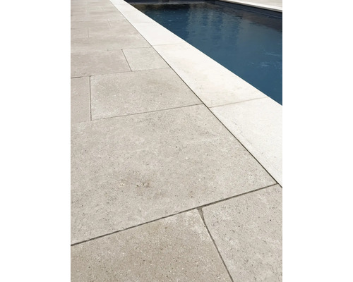 Großformatige Terrassenplatten aus Naturstein neben einem Swimmingpool, strukturierte Oberfläche, helle Poolumrandung.