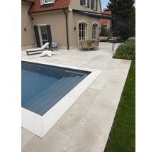 Großflächige Poolterrasse aus hellen Steinplatten mit Essbereich und Sonnenliegen im Garten eines Hauses.