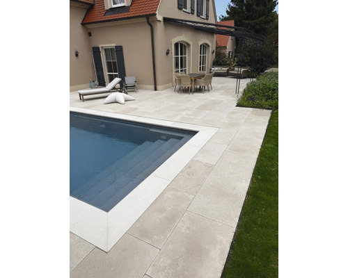 Großflächige Poolterrasse aus hellen Steinplatten mit Essbereich und Sonnenliegen im Garten eines Hauses.