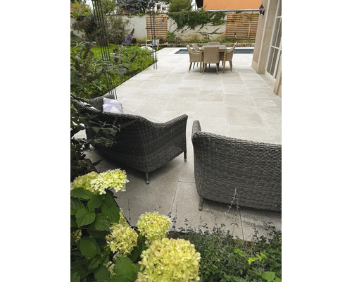 Helle Terrasse mit Steinplatten im Großformat, Geflecht-Lounge-Sesseln, Sitzgruppe und Garten mit Pflanzen. Organisiert gestaltet.