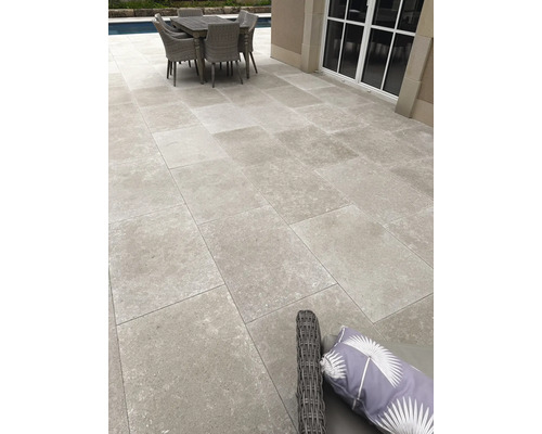 Moderne Terrasse mit Feinsteinzeugplatten in Steinoptik, Sitzgruppe und Pool im Hintergrund.