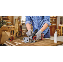 Ein Mann benutzt eine Nutfräse, um ein Werkstück zu bearbeiten. Auf dem Tisch liegen Holzplättchen und eine Flasche Klebstoff.