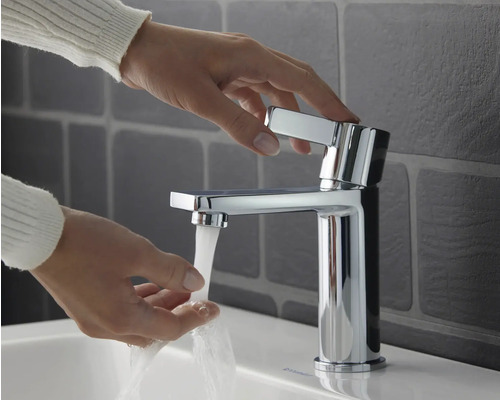 Person bedient einen glänzenden Waschtischmischer im Badezimmer