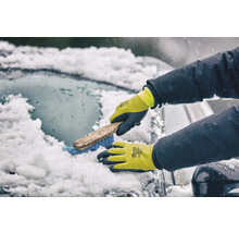 Person mit Winterhandschuhen reinigt eine verschneite Autoscheibe mit einer Bürste.