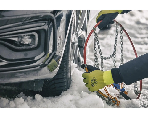 Person montiert Schneeketten an einem Autoreifen im Winter