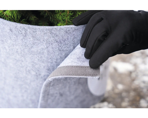 Eine Hand mit Handschuh befestigt einen Wurzelschutzsack an einer Pflanze.