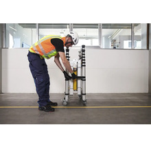 Eine Person sichert ein zusammengeklapptes Rollgerüst mit einem Gurt.