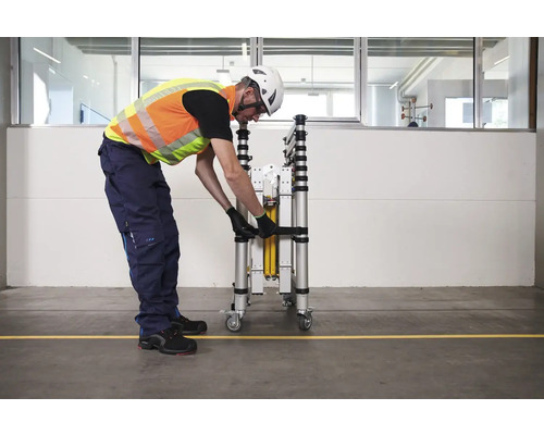 Eine Person sichert ein zusammengeklapptes Rollgerüst mit einem Gurt.