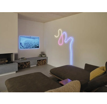 Modernes Wohnzimmer mit Kamin, Fernseher und einer geschwungenen LED-Wandbeleuchtung in Neon-Optik über einem Sofa.