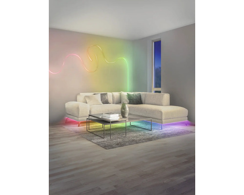 Modernes Wohnzimmer mit wellenförmigem LED-Lichtstreifen an der Wand, beleuchtetem Ecksofa und Couchtisch auf einem Teppich.