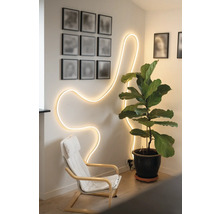 Hell beleuchteter Raum mit flexiblem LED-Lichtschlauch in Wellenform an der Wand, einem Sessel und einer großen Zimmerpflanze im Topf.