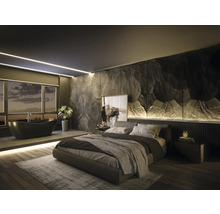 Modernes Schlafzimmer mit integriertem Bad, Akzentwand in Steinoptik, freistehender schwarzer Badewanne und Polsterbett auf Holzboden.