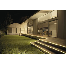 Modernes Haus bei Nacht mit LED-Streifen zur Beleuchtung der hölzernen Treppenstufen und der Terrasse am Rasen.