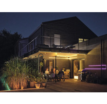 Beleuchtete Holzterrasse bei Nacht mit Personen am Esstisch, Grill und LED-Lichtstreifen unter dem Balkon sowie entlang der Bodenkante.