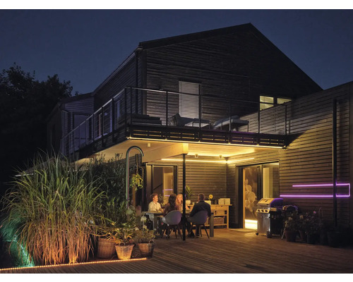 Beleuchtete Holzterrasse bei Nacht mit Personen am Esstisch, Grill und LED-Lichtstreifen unter dem Balkon sowie entlang der Bodenkante.
