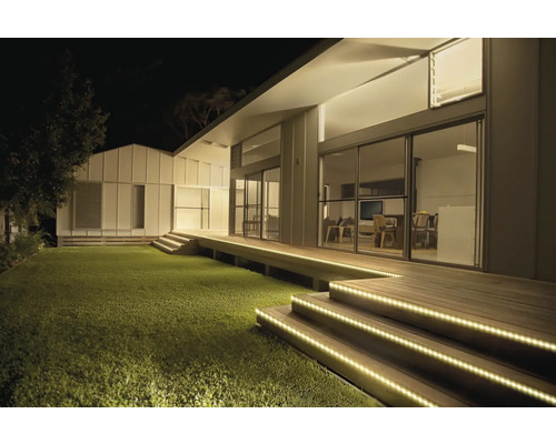 Modernes Haus bei Nacht mit LED-Streifen zur Beleuchtung der hölzernen Treppenstufen und der Terrasse am Rasen.