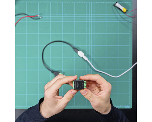 Eine Person hält ein kleines schwarzes Analog-Add-on-Elektronikmodul mit grünen Anschlüssen über einer Arbeitsfläche.