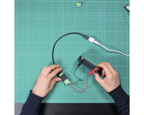 Hände montieren elektronische Bauteile und Kabelverbindungen mit Krokodilklemmen auf einer Arbeitsunterlage.