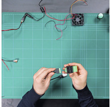 Hände verbinden ein Kabel mit einem SSR ADDON Modul auf einer Arbeitsfläche mit elektronischen Bauteilen wie Lüfter und Kabeln.
