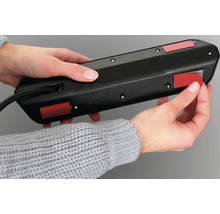 Eine Person befestigt eine Steckdosenleiste mit Klebestreifen.