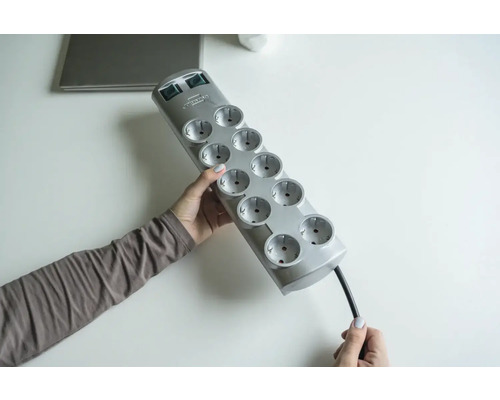 Eine Person hält eine graue Steckdosenleiste mit zehn Steckplätzen.