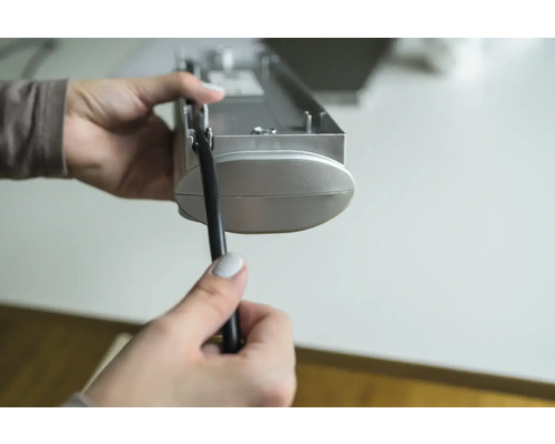 Eine Person hält eine Jalousie und eine Zugschnur in der Hand.