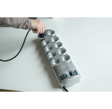 Person steckt Stecker in eine graue Steckdosenleiste mit zehn Steckplätzen