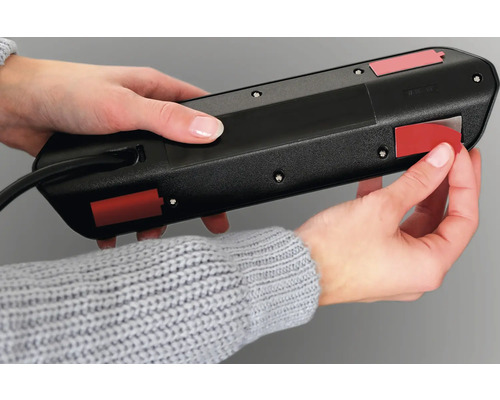 Eine Person befestigt eine Steckdosenleiste mit Klebestreifen.