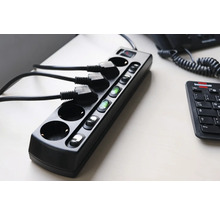 Schwarze Steckdosenleiste mit Schaltern und eingesteckten Kabeln auf einem Tisch