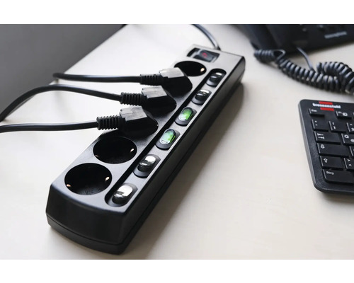 Schwarze Steckdosenleiste mit Schaltern und eingesteckten Kabeln auf einem Tisch