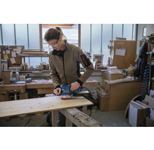 Eine Person schleift ein Holzbrett mit einem Exzenterschleifer in einer Werkstatt.