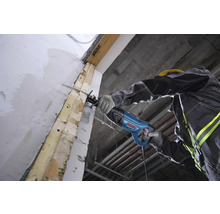 Ein Handwerker schneidet mit einer Bosch Professional Säbelsäge einen Holzbalken an einer Wand auf einer Baustelle.